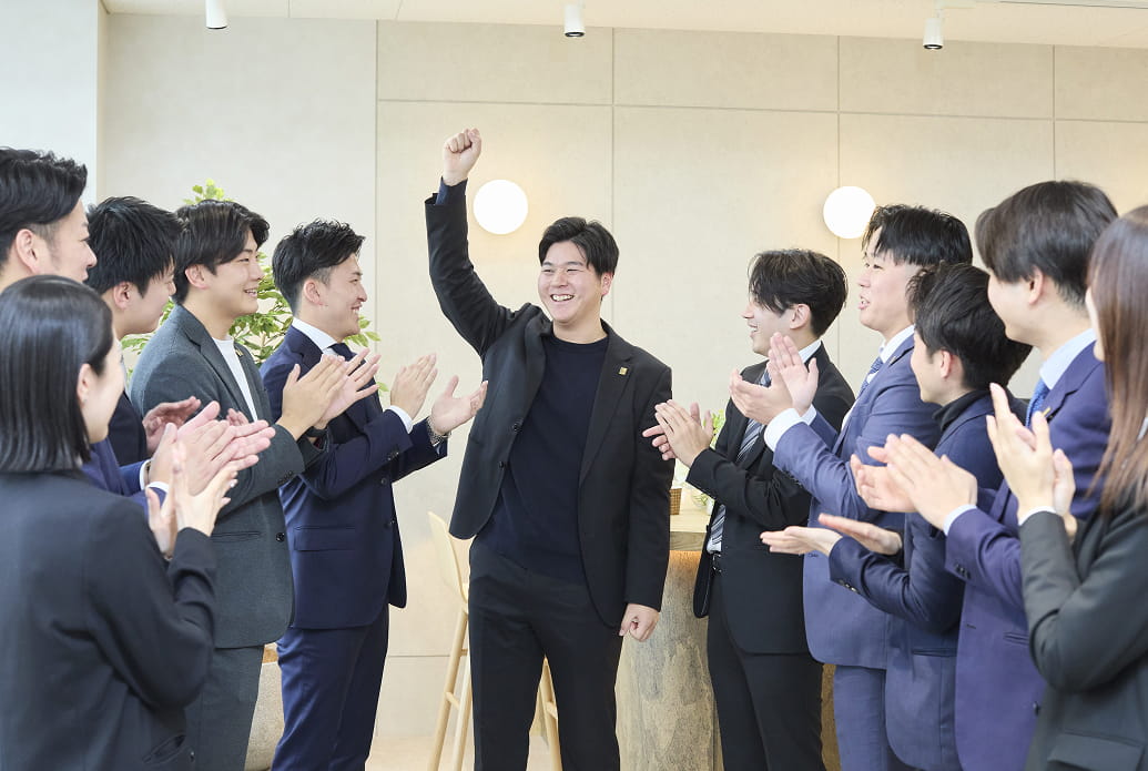 1人の男性がガッツポーズして、他の社員が拍手をしている様子