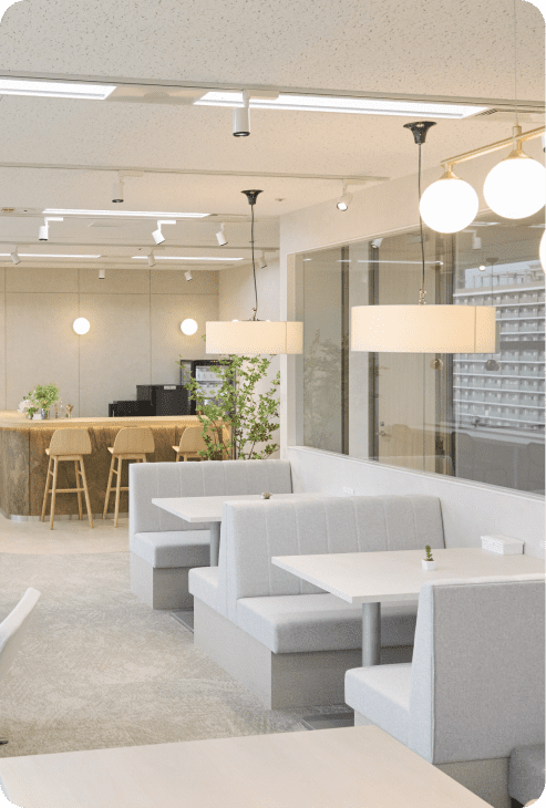 モダンなオフィスのラウンジエリア。ボックスシートとテーブルが並び、奥にはカウンター席がある。